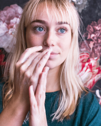 Meid met blond haar en blauwe ogen wrijft handcrème van NatuurlijkWAAR op haar handen