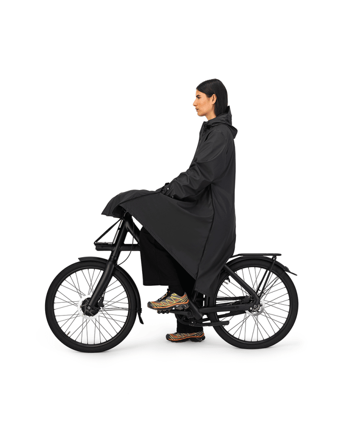 vrouw op fiets met maium regenjas van gerecyclede petflessen in de kleur black zwart uitgevouwen tot regenponcho zijaanzicht