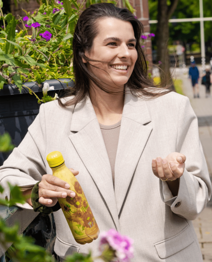 lachende vrouw in blazer met de thermosfles zonnebloemen van gogh van izy bottles in haar hand